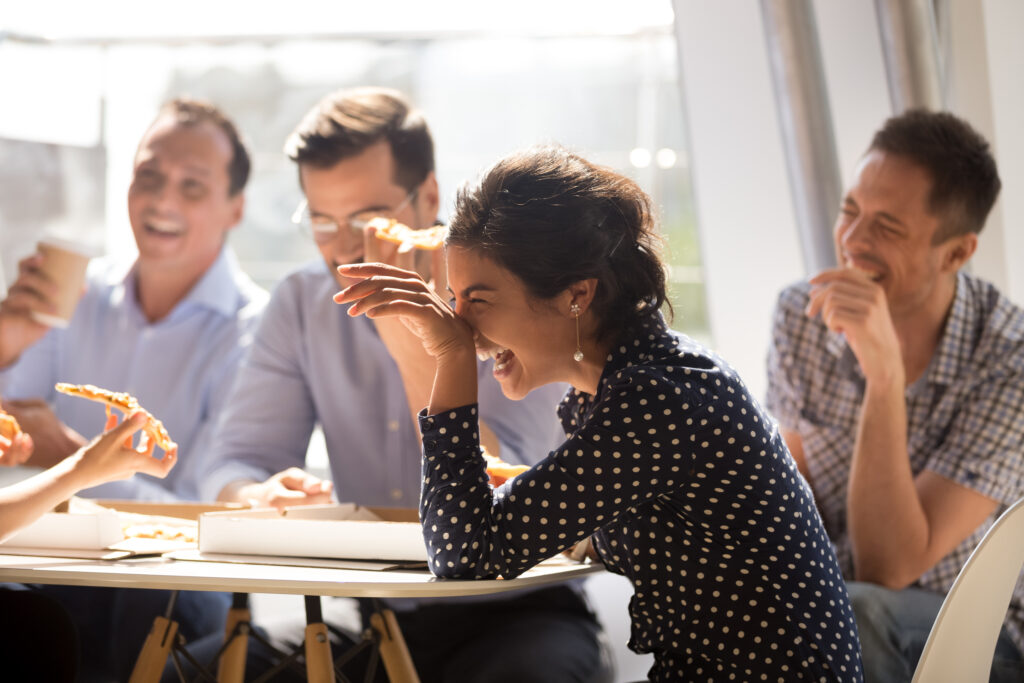 Indian woman laughing eating pizza with diverse coworkers in off